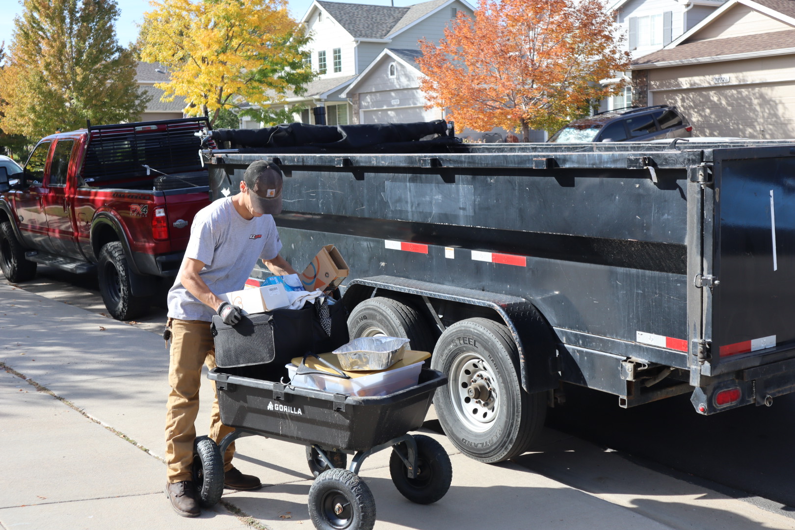 EZ Haulaway crew member loading household junk from a cart into the black dump trailer beside the red work truck, a dumpster rental alternative