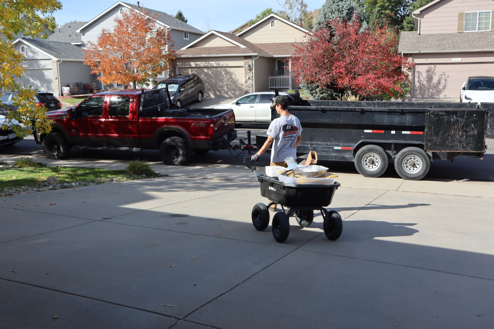 EZ Haulaway crew member wheeling a cart of boxes from a storage unit cleanout toward the black dump trailer behind the red work truck